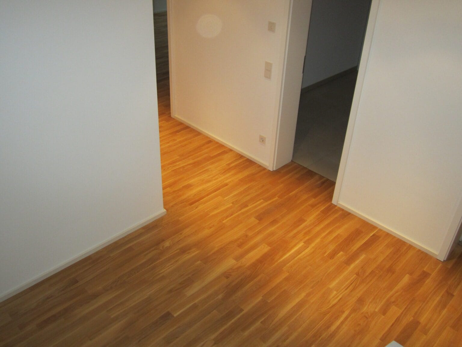Flur mit neuem Boden in warmem Holzton und weißen Sockelleisten