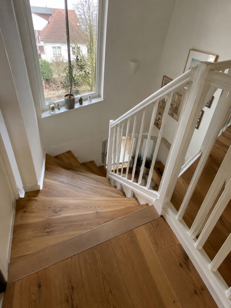 Blick von oben auf eine gewendelte Holztreppe mit weißem Geländer