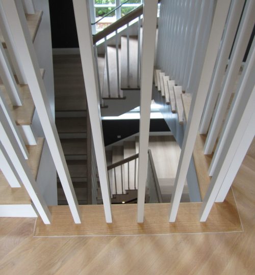 Blick durch ein weißes Treppengeländer auf Eichenparkett und Holztreppe